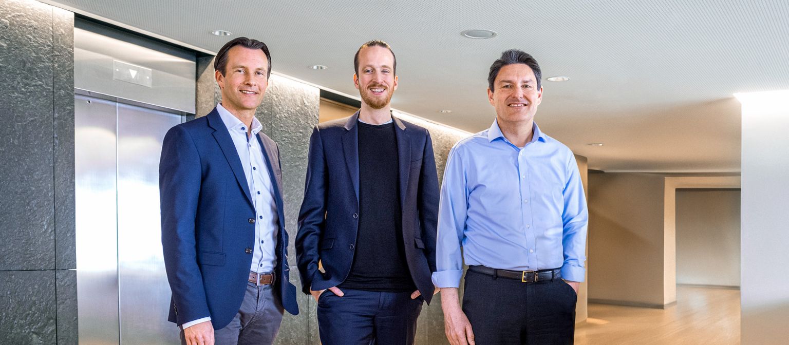 Three male members of the EOS Group’s Board of directors are standing in business attire in front of elevators in a modern setting.