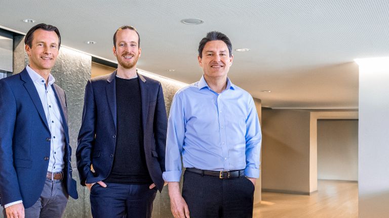 Trois membres masculins du conseil d'administration du Groupe EOS se tiennent en tenue professionnelle devant des ascenseurs dans un cadre moderne.