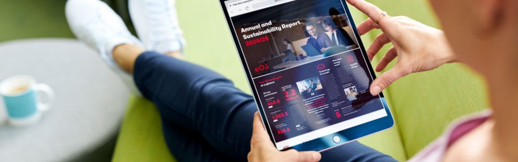 Osoba na zelené pohovce prohlížející si Výroční zprávu a Zprávu o udržitelnosti EOS 2024/25 na tabletu
