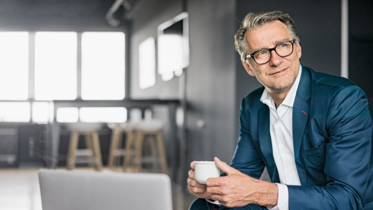 Portrét sediaceho zrelého podnikateľa v modrom obleku, ktorý drží bielu šálku kávy