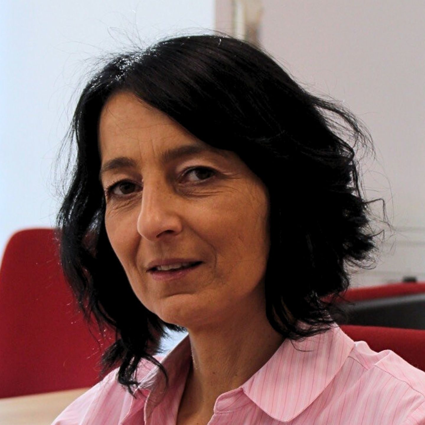 Cristina Pasere, menadžer za podršku operacijama usklađenosti u EOS Romania, sjedi za svojim stolom u ružičastoj prugastoj bluzi i gleda u kameru.