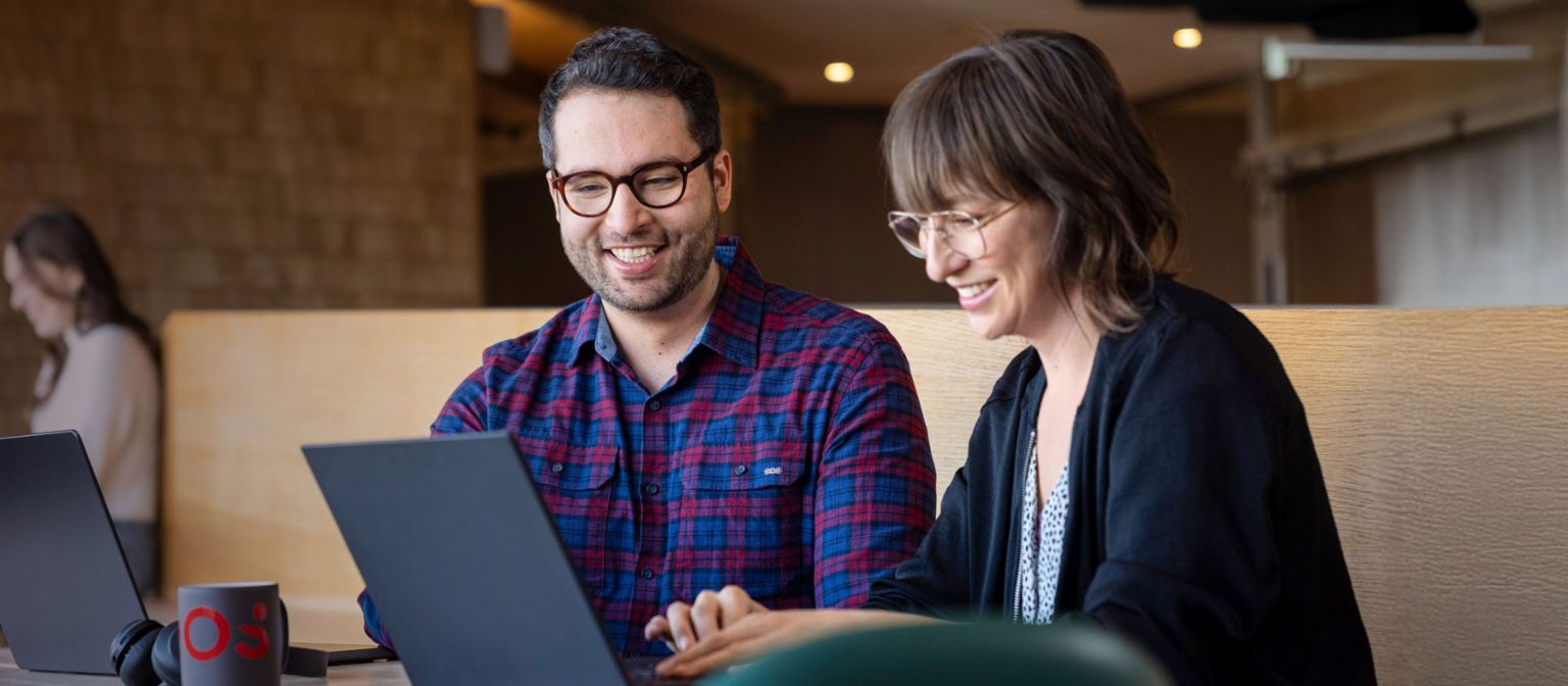 Deux collaborateurs d'EOS regardent ensemble un ordinateur portable tout en étant absorbés par une conversation.