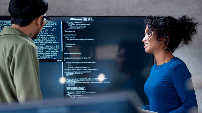 AI v inkase: Na tomto obrázku dvaja profesionáli spoločne analyzujú programový kód pre automatizované procesy na veľkom displeji. Scéna ilustruje praktickú aplikáciu umelej inteligencie (AI) a robotizovanej automatizácie procesov (RPA) v správe dlhov – príklad digitálnej transformácie v správe pohľadávok.