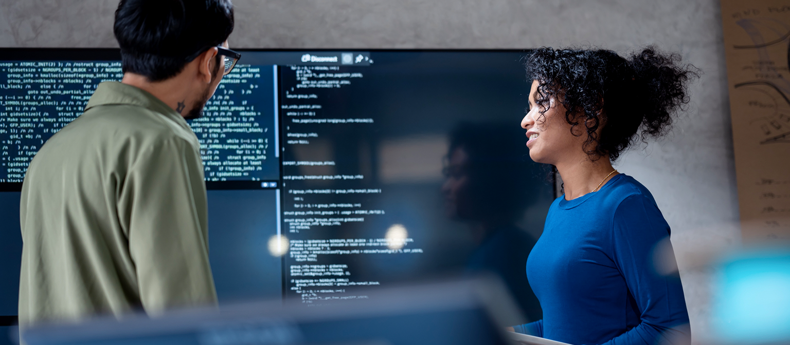 AI in debt collection: In this image, two professionals are collaboratively analyzing program code for automated processes on a large screen. The scene illustrates the practical application of Artificial Intelligence (AI) and Robotic Process Automation (RPA) in debt management – an example of digital transformation in receivables management.