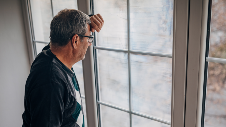 Fair debt collection: A middle-aged male debtor in an olive-colored jacket looks out the window with concern.