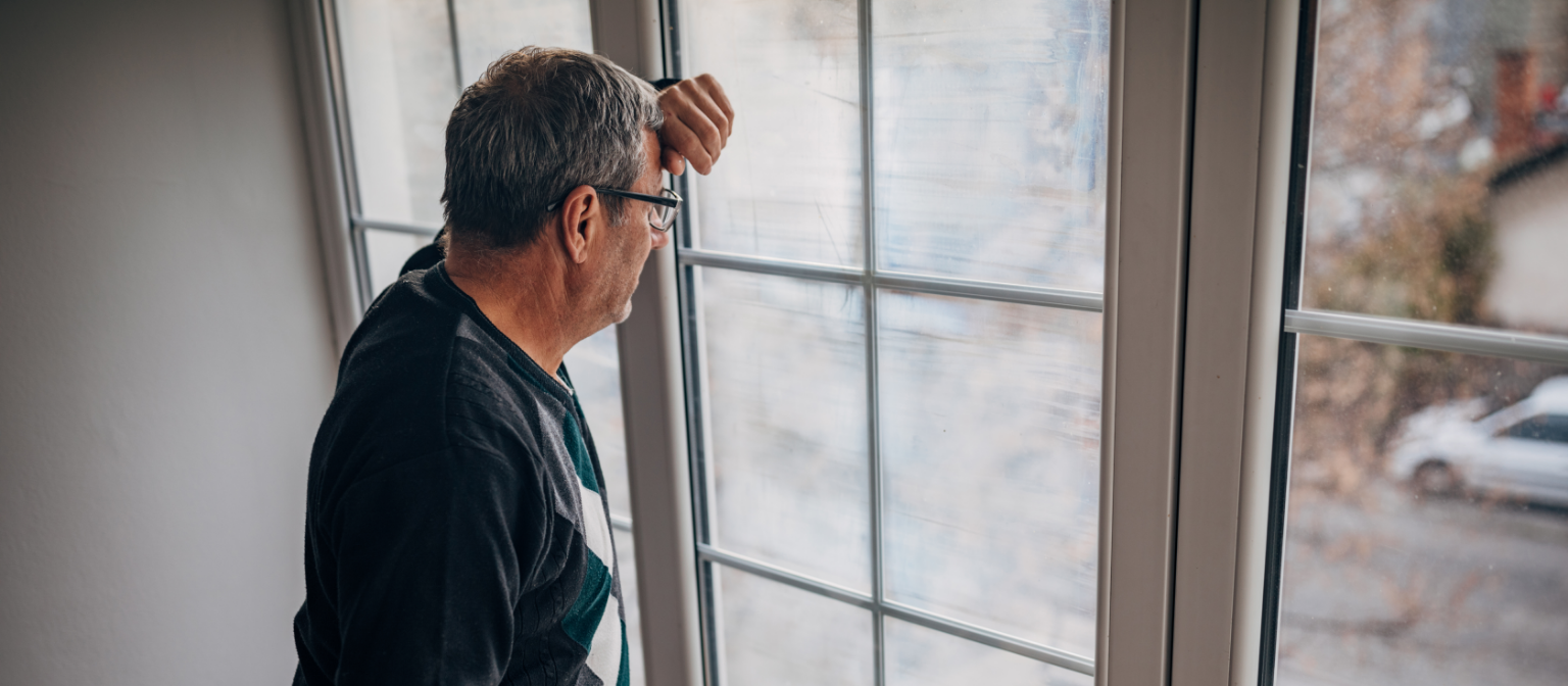 Fair debt collection: A middle-aged male debtor in an olive-colored jacket looks out the window with concern.