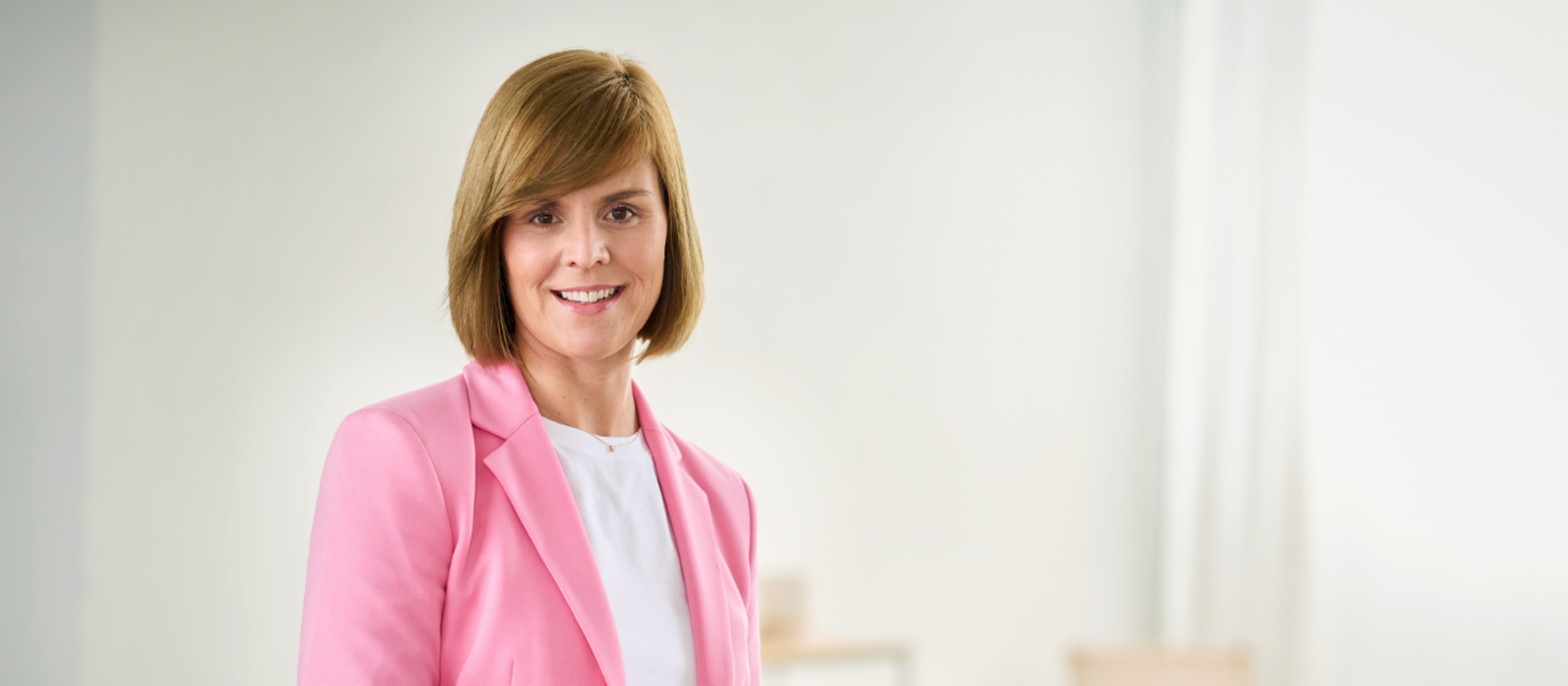 Eva Griewel, žena u ružičastom blejzeru i bijeloj košulji stoji u svijetloj prostoriji